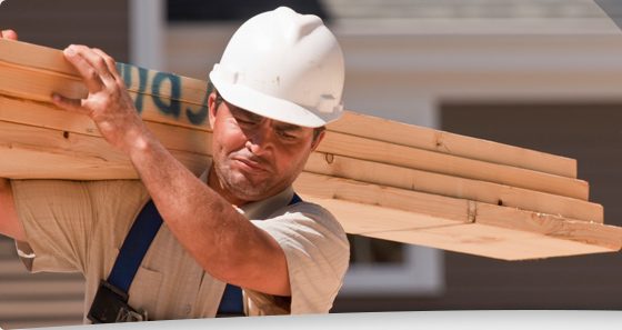 A construction worker carrying lumber on his shoulder