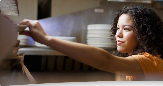 A restaurant worker reaching for dishes in a commercial kitchen